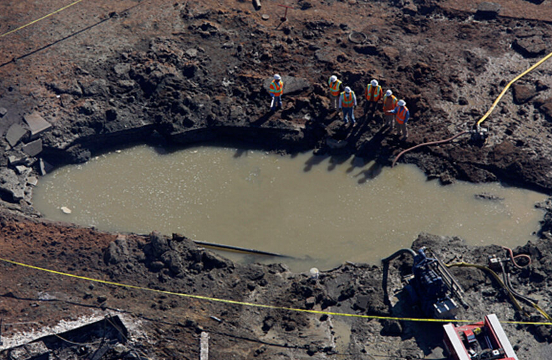 workers looking at at hole filled with water